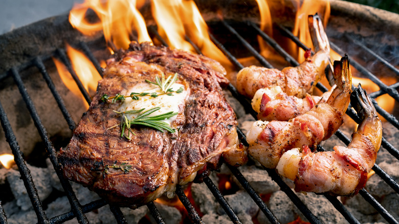 a butter-topped steak and bacon-wrapped chrimp on a flaming charcoal grill