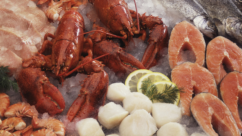 shrimp, lobsters, scallops, and several types of fish laid out on ice with lemon slices and fresh dill