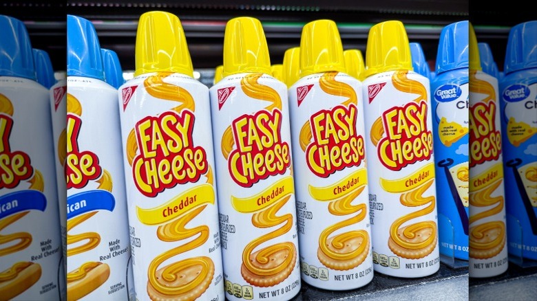 Multiple cans of Easy Cheese Cheddar Cheese Spray on a shelf