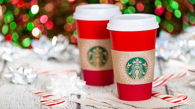 Two Starbucks red cups with candy canes and Christmas lights