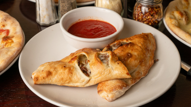 A stromboli on a silver platter, beside a small tub of marinara dipping sauce