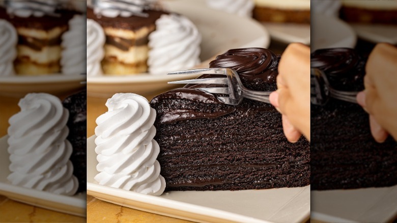 A fork sinking into a slice of Linda's Fudge Cake with whipped cream on the side