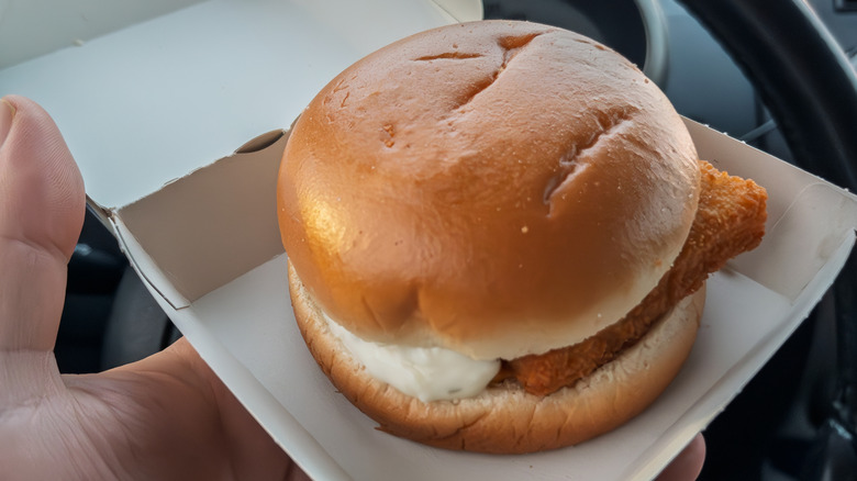 A McDonald's Filet-O-Fish sandwich in a cardboard container held by someone in a car