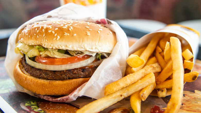 A Whopper, wrapped in paper, sitting on a fast food tray beside an order of fries