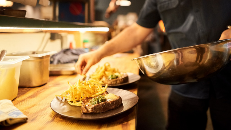 A chef plates steak frites with fries and greens