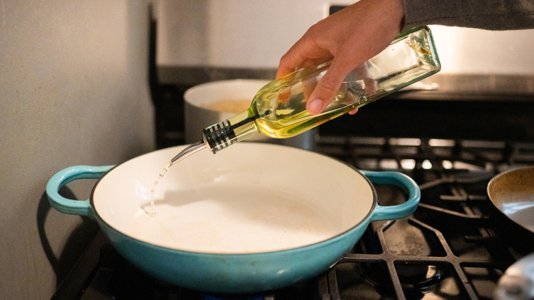 Person pours cooking oil from glass container into saucepan on stove