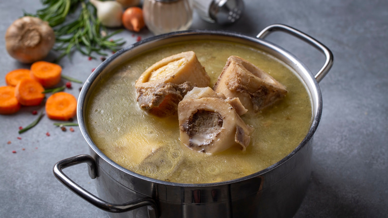 Stock pot with large beef bones simmering, aromatics in the background