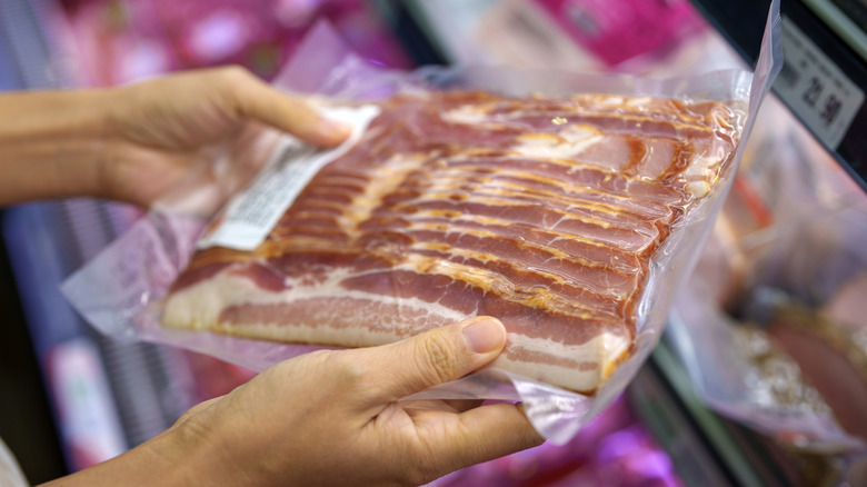 Woman holding a vacuum-sealed pack of bacon.