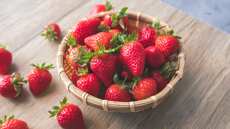 A bamboo bowl full of strawberries on a wooden table