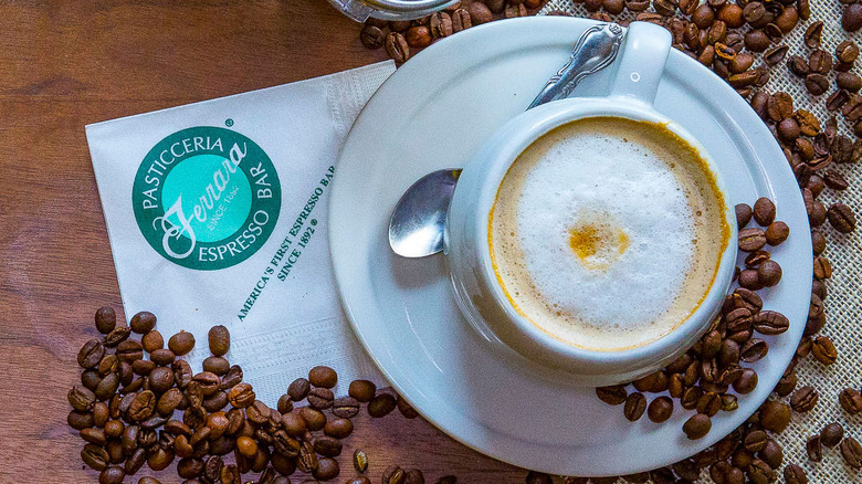 A cappuccino surrounded by espresso beans and a Ferrara napkin