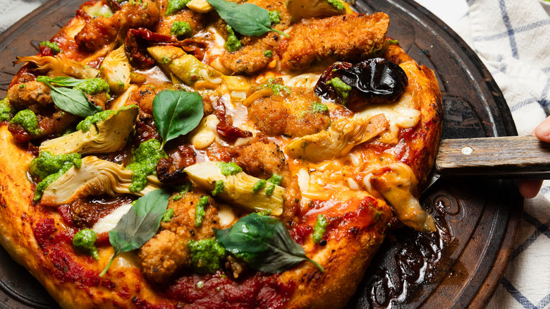 A slice of pizza on plate with larger pizza behind it