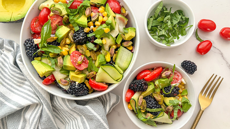Bowls of salad with avocado, tomatoes, blackberries, and basil