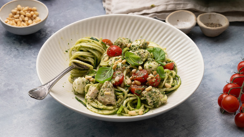 Bowl of pesto chicken and zucchini noodle salad with cherry tomatoes and basil
