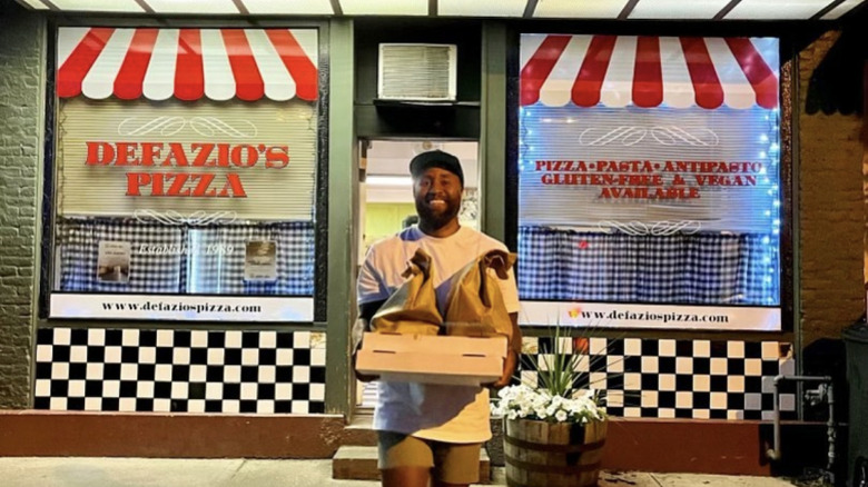 A man holding to-go bags and a pizza box in front of DeFazio's Wood Fire Pizza