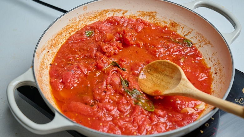 spoon crushing tomatoes in a skillet