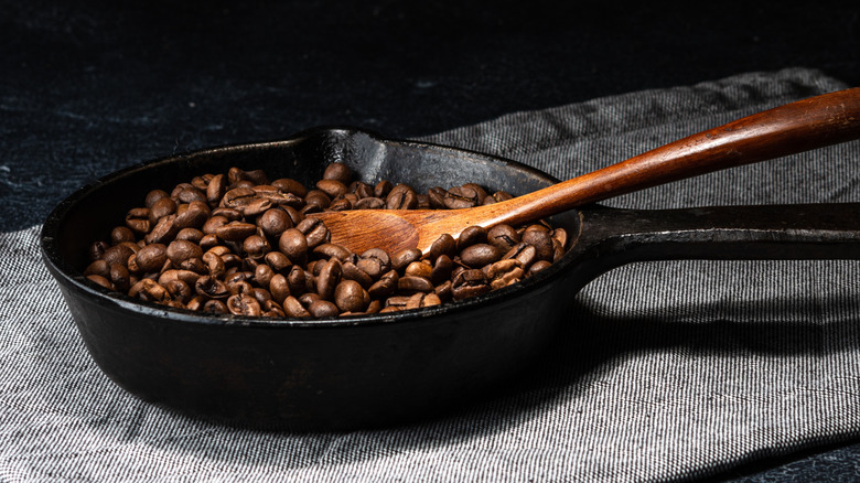 Roasted coffee beans in a cast iron skillet with a wooden spoon