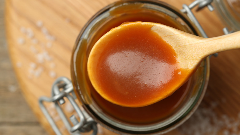 Wooden spoon full of caramel sauce above glass jar