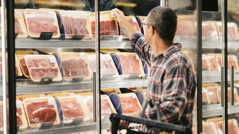 A man with glasses in a plaid shirt taking beef out of a store fridge