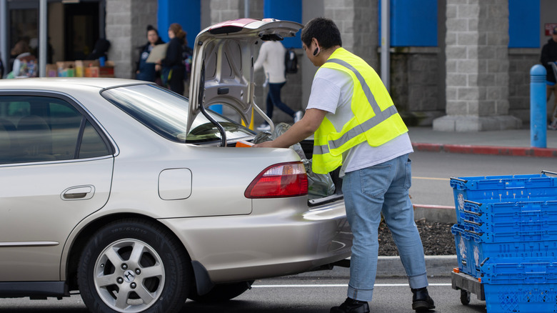 Walmart employee loading car trunk with curbside pickup groceries