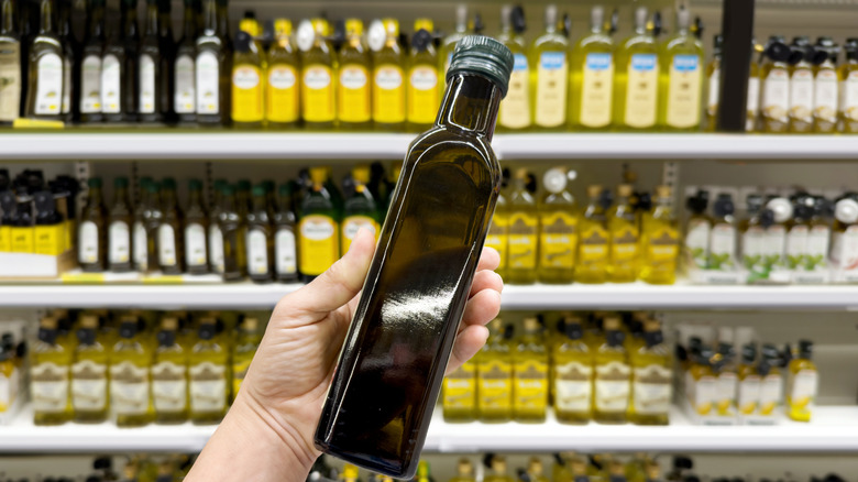 Someone holding up an unlabeled bottle of olive oil in front of shelf at the grocery store