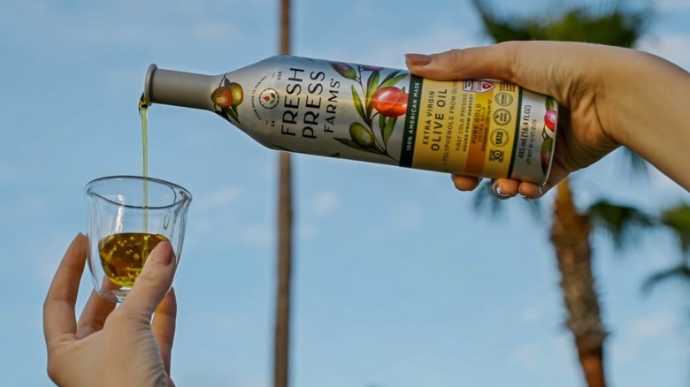 woman pouring bottle of Fresh Press Farms olive oil into a small glass cup