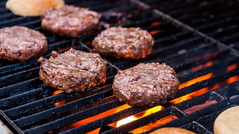Burgers cooking on the grill with buns toasting beside them