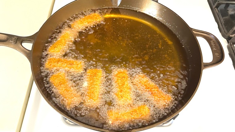 Mozzarella sticks frying in oil in Made In seasoned cast iron 12" skillet