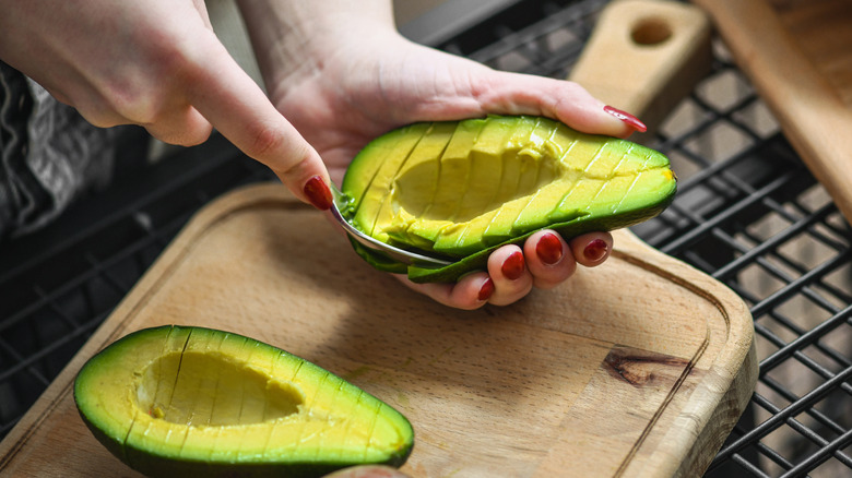 Scooping out sliced avocado half on cutting board