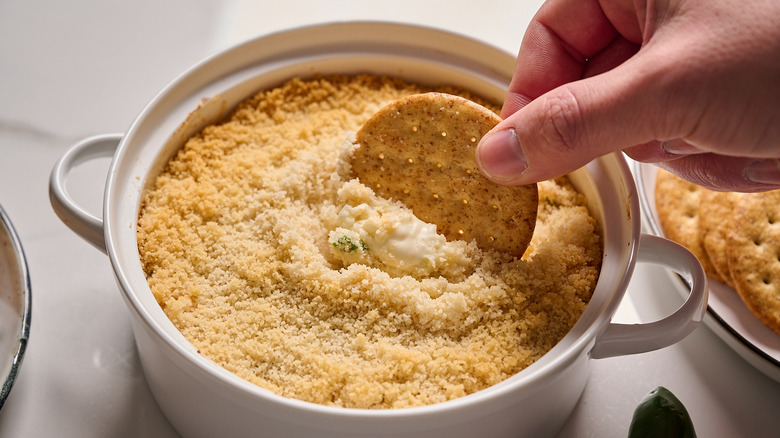 dipping cracker into a jalapeno popper dip
