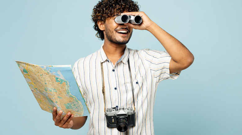 Person holding map, carrying camera, and looking through binoculars