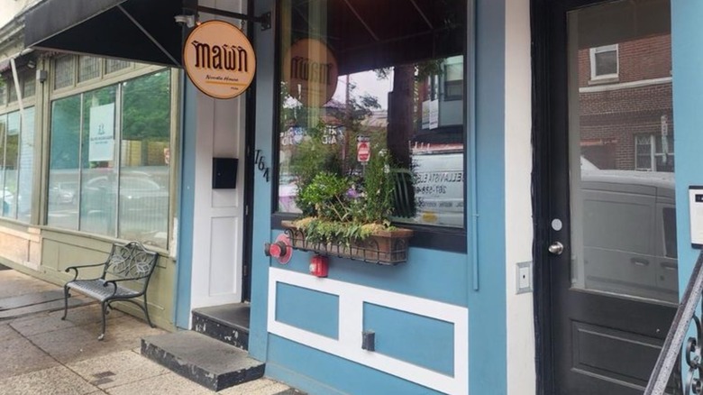 Exterior of Mawn blue storefront with flowerbox and small sign