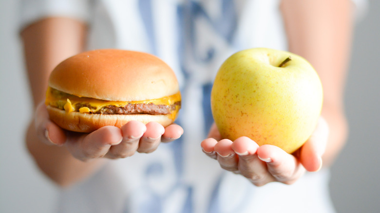 Person holding a burger and an apple