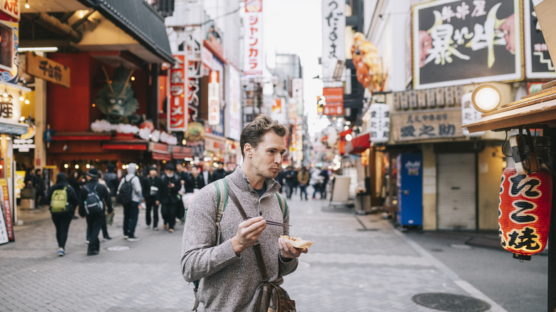 Caucasian tourist eating take out food on a busy street in Japan