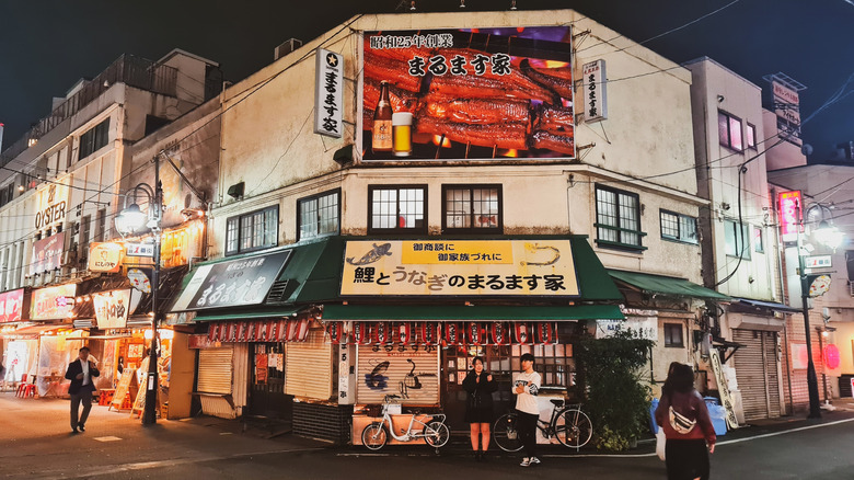 A street in Japan with restaurants that are closed, a few people walking down the street