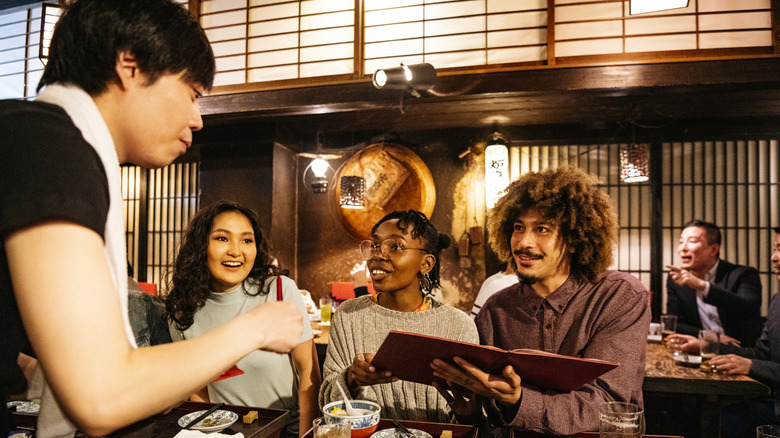 Tourists at a Japanese restaurant asking the waiter about the menu, four people two women and two men