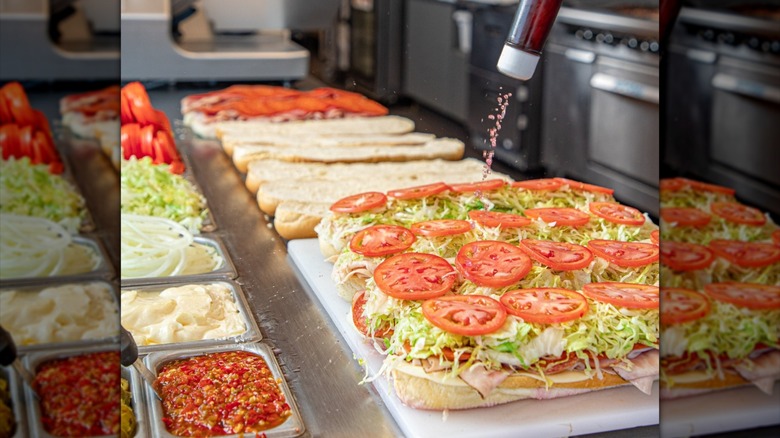 Jersey Mike's employee dressing row of open-face sub sandwiches