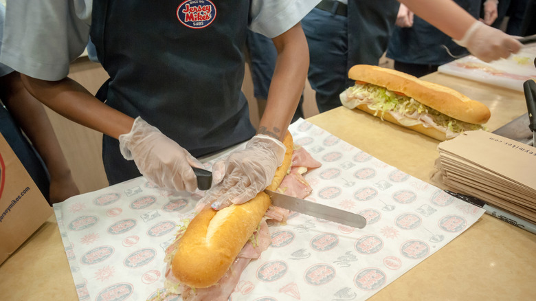 Jersey Mike's employee slicing a prepared sub sandwich in half