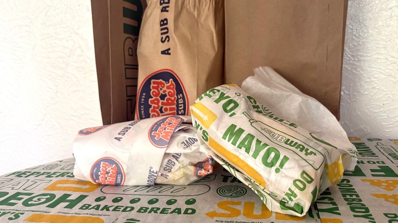 Wrapped sub sandwiches with paper bags in background