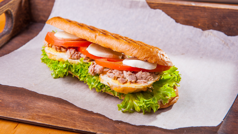 A tuna sub sitting on a white piece of tissue paper on a wooden counter