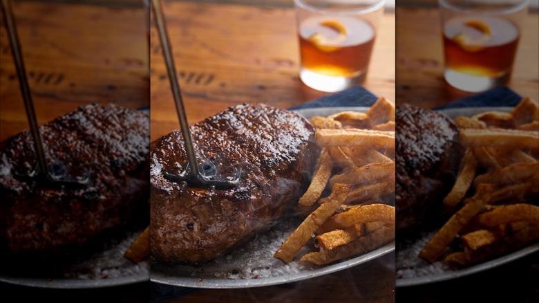 A steak being branded on a tray beside fries and a drink