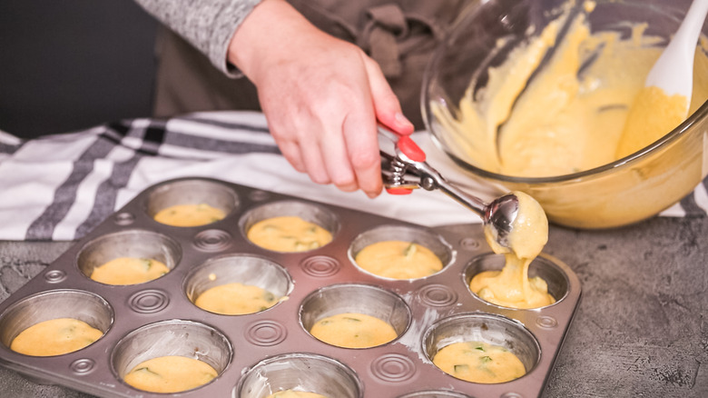 A person scooping cornbread batter into a muffin tray