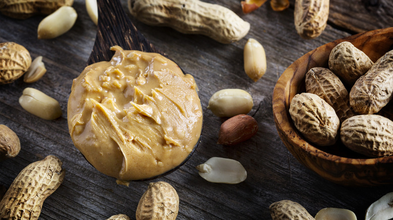 A wooden spoon full of peanut butter besides shelled and whole peanuts