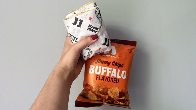 Hand holding Jimmy John's Buffalo Ranch Chicken Wrap and Buffalo-flavored chips
