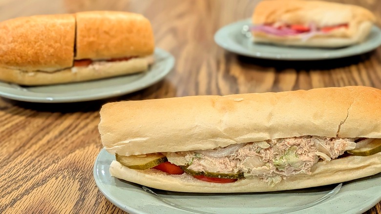 A close-up of a tuna sub from Jimmy John's with two other subs in the background, all on light blue plates