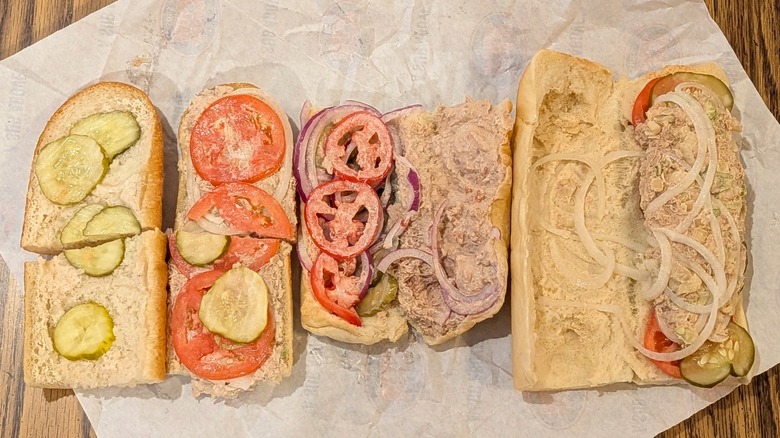 Three open-faced tuna subs with tomato, onion, and pickles on white paper