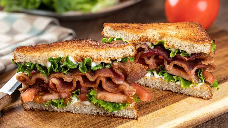 BLT sandwich sliced in half on wooden cutting board