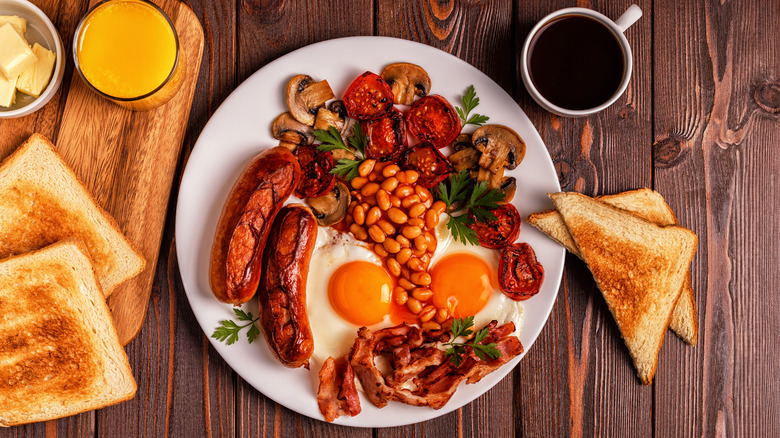 A full english breakfast on a plate surrounded by coffee, orange juice, and toast