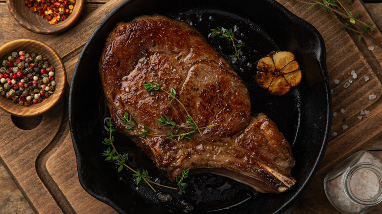 a cowboy steak on a cast iron pan with fresh thyme and a head of garlic
