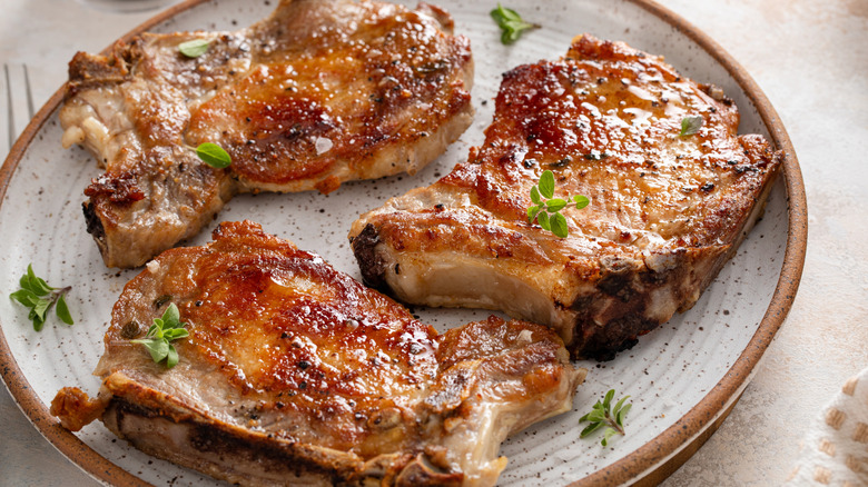 A plate of cooked pork chops garnished with fresh herbs