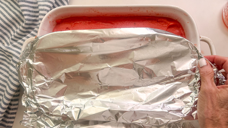 hands covering dish with foil